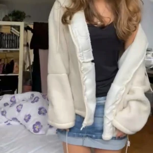 Vit fleece teddyjacka med huva - Mysig vit teddyjacka i fleece med huva och dragkedja framtill. Jackan har en loose passform och snörning nedtill för att justera stilen. Perfekt för dig som gillar chill och comfy vibes. Långärmad och enkel att matcha med jeans eller kjol.