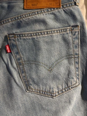 Levi's 501 ljusblå jeans straight fit - Ljusblå Levi's 501 jeans med klassisk röd Levi's-tag på bakfickan och brunt läderpatch i midjan. Modellen har rak passform och är tillverkad i slitstarkt bomullsjeansmaterial. Perfekt för dig som gillar tidlös och avslappnad stil. Priset går att diskuteras!