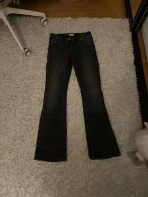 Svarta bootcut jeans med rosett-detalj - Säljer ett par svarta jeans från Gina tricot med bootcut-snitt och snygga rosett-detaljer och paljetter på bakfickorna. Jeansen har klassisk femficksdesign, kopparfärgade knappar och dragkedja. Materialet är jeans med en mörk tvätt som ger en cool vibe.