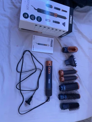 Princess AirStyler 7-i-1 stylingverktyg - Princess AirStyler 7-i-1 är ett multifunktionellt stylingverktyg i svart och kopparfärgad plast och metall. Setet innehåller flera utbytbara borstar och munstycken för olika hårstylingar, inklusive rundborstar och volymmunstycke. Perfekt för att skapa olika looks med ett enda verktyg.