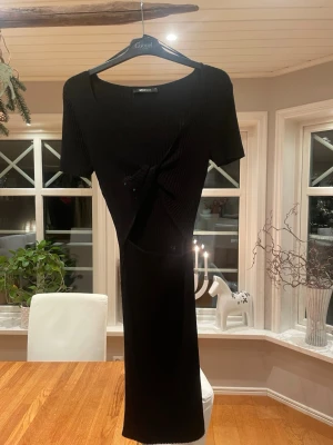Svart ribbad långklänning Gina Tricot - Säljer en svart ribbad långklänning från Gina Tricot i storlek XS. Klänningen har korta ärmar, omlottdetalj framtill och är figurnära med snygg struktur. Perfekt för dig som gillar stilrena och trendiga plagg med twist.