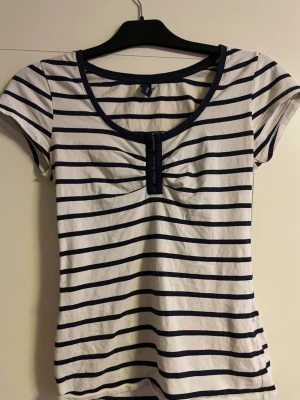 Randig topp från 365 Sunshine, S - Säljer en vit och marinblå randig topp från 365 Sunshine i storlek S. Toppen har korta ärmar, rund halsringning och knappar framtill. Materialet är mjuk bomull och passformen är normal. Perfekt för dig som gillar klassisk stil med en twist. Den har lite missfärgningar under armhålan men de är inget man tänker på💗