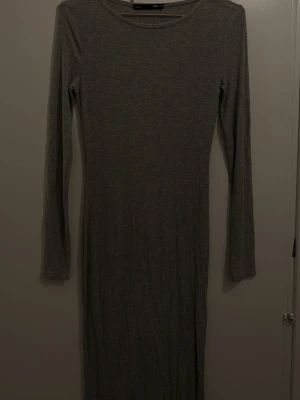 Grå ribbad långklänning från 157 - Säljer en enkel och stilren grå långklänning från 157 i storlek XS. Klänningen har ett ribbat tyg, rund halsringning och långa ärmar. Perfekt för dig som gillar minimalistisk och bekväm stil.