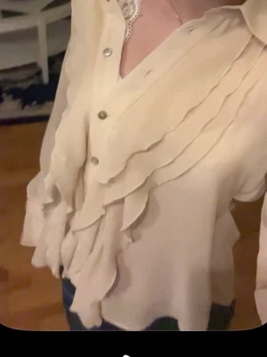 Vit/beige volangblus - Så fin vit/beige volangblus som endast använts en gång (alla bilder är från samma tillfälle) blusen är i väldigt tunnt material och är lite genomskinligt. Så fin både till jeans eller shorts!