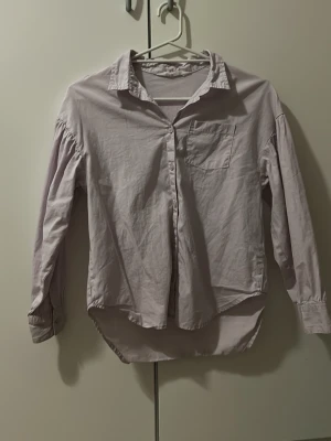 Ljuslila skjorta från H&M - Säljer en ljuslila skjorta från H&M i storlek 140. Skjortan har klassisk krage, knappstängning framtill och en bröstficka. Långärmad med knappar vid ärmslut och något längre baktill för en cool look. Perfekt att styla med jeans eller kjol. Kontakta mig för pris förslag!