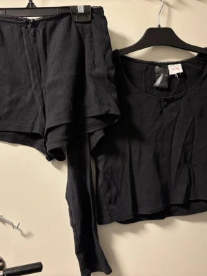 Svarta shorts från H&M i bomull - Svarta shorts från H&M i mjuk bomull med diskret ribbad struktur. De har en relaxed fit och elastisk midja, perfekta för chill dagar. Matchar enkelt med andra plagg och har en enkel, stilren look.