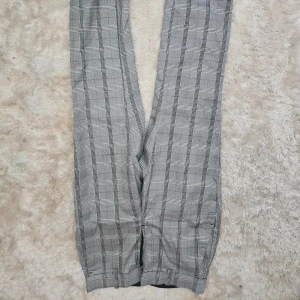 Grå rutiga kostymbyxor H&M, strl 36 - Snygga grå kostymbyxor från H&M i storlek 36. Byxorna har ett klassiskt rutigt mönster och raka ben. Perfekta för en stilren look och passar till många olika outfits.