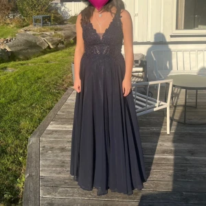 Mörkblå långklänning med spetsdetaljer - Säljer en elegant mörkblå långklänning med djup v-ringning. Perfekt för val eller festliga tillfällen. Använd en gång, nypris runt 4000 och köpt på Johans Högtidskläder i Göteborg. Jag är 162 och har på mig en låg klack. Till klänningen finns också ett strassband som sitter i midjan. Undrar ni något är det bara att fråga 💕💕 påse ingår.