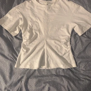 Vit kortärmad topp i bomull - Enkel och stilren vit topp med korta ärmar och rund hals. Toppen har en rak passform och en synlig söm som går rakt ner i mitten både fram och bak. Perfekt basplagg i mjuk bomull som funkar till allt.