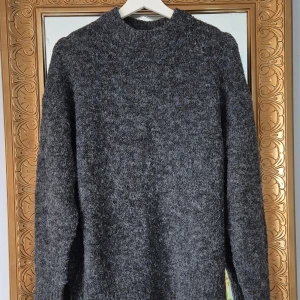 Mörkgrå stickad tröja - Mörkgrå stickad tröja med hög hals och långärmad modell. Rimlig I storlek den passar S-M