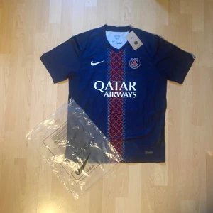 PSG matchtröja D.Doué #14 Nike - Säljer en officiell Paris Saint-Germain fotbollströja med D.Doué och nummer 14 på ryggen. Tröjan är marinblå med röd och vit grafisk detalj på framsidan, har korta ärmar och är tillverkad i lätt polyester. Nike-logga och Qatar Airways tryck på bröstet.