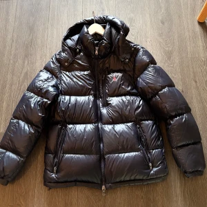 Svart pufferjacka från Polo Ralph Lauren - Säljer en mörkblå pufferjacka från Polo Ralph Lauren i storlek L. Jackan har huva, två stora dragkedjefickor. perfekt för kalla dagar. Köptes förra vintern och användes sparsamt.