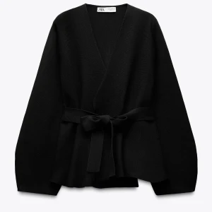 Svart cardigan jacka från Zara - Stilren svart cardigan  från Zara med omlottknäppning och brett knytband i midjan. Jackan har lång ärm, v-ringad hals och en loose passform som ger en avslappnad men ändå chic look. Perfekt för lager-på-lager och enkel att matcha.