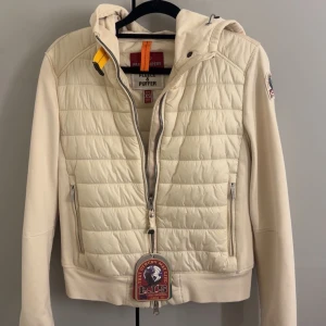 Beige pufferjacka från Parajumpers XS - Snygg beige pufferjacka från Parajumpers med huva och dragkedja. Jackan har quiltad framsida och rygg, släta ärmar och coola detaljer som logopatch på ärmen och gul rem vid halsen. Perfekt för dig som vill ha en stilren och sportig look. Köpt för 3800kr Säljs för 2700kr pris kan diskuteras vid snabb affär