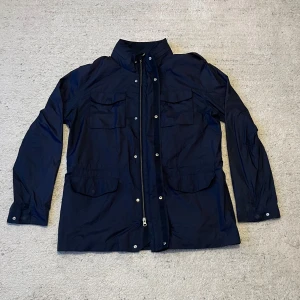 Boggi Milano jacka - Säljer en snygg lite längre mörkblå jacka från Boggi Milano. Den har en stilren design med dragkedja och knappar framtill. Jackan har flera praktiska fickor och är perfekt för höst och vår. Perfekt för dig som vill ha en klassisk look! 