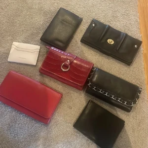 Mix av plånböcker och kuvertväskor i skinn - Säljer ett gäng snygga plånböcker och kuvertväskor i svart, rött och vitt skinn. En röd med croco-mönster och metallring, en svart med kedjedetalj, samt en vit kortplånbok från Don Donna. Perfekt för dig som gillar stilrena accessoarer. Helt nya. 100 kr st. Endast swish betalning