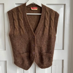 Brun stickad väst från Valentino Miss V - Brun stickad väst från Valentino Miss V med grova flätstickade detaljer framtill och bak. Västen har v-ringning, tre knappar framtill och två fickor. Tillverkad i ull 🤎