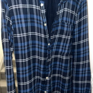 Blå och svart rutig skjorta från Knowledge Cotton Apparel - Snygg blå och svart rutig flanel skjorta från Knowledge Cotton Apparel. Skjortan är Perfekt för en avslappnad stil med en klassisk touch. Ett måste i garderoben nu i vinter ❄️ pris kan diskuteras vid snabb affär!