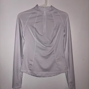 Vit långärmad träningströja half zip - Superskön vit långärmad träningströja med half zip framtill och tumhål i ärmsluten. Tröjan är i ett stretchigt syntetmaterial som andas och har en slim passform. Perfekt för löpning eller gymmet när du vill ha något lätt men täckande.