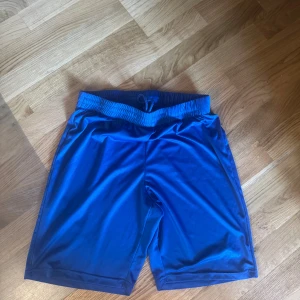 Blå träningsshorts med snörning - Snygga blå träningsshorts med elastisk midja och snörning framtill. De är tillverkade i ett mjukt och lätt syntetmaterial som andas bra, perfekta för gymmet eller sport. Klassisk passform och stilren design utan mönster. 