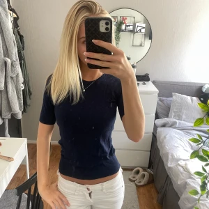 Mörkblå ribbad topp med kort ärm - Säljer en mörkblå, tight ribbad topp med rund hals och korta ärmar. Enkel och stilren modell som sitter figurnära och har en mjuk känsla. Perfekt att matcha med jeans eller kjol för en clean look.