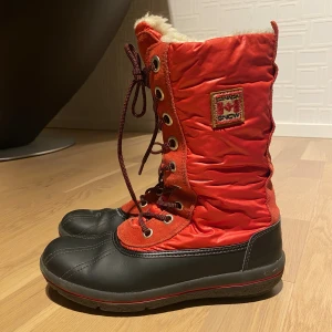 Röda vinterstövlar från Canada Snow - Snygga vinterstövlar från Canada Snow i rött och svart med snörning framtill och dragkedja bak. Ovandel i syntet och mocka, fodrad insida och slitstark gummisula. Perfekta för kalla dagar med sin varma och coola look. Pris kan diskuteras!