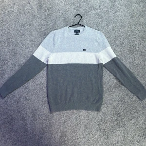 Gråvit stickad tröja från Lexington - Snygg stickad tröja från Lexington i grått och vitt med breda blockränder. Tillverkad i ekologisk bomull och har rund halsringning samt diskret logga på bröstet. Perfekt för dig som gillar stilren och enkel design.