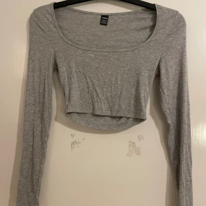 Grå croppad långärmad topp från SHEIN - Säljer en enkel och stilren grå croppad topp från SHEIN. Toppen har lång ärm, rundad urringning och är tillverkad i mjuk bomullsblandning. Perfekt att matcha med höga jeans eller kjol för en clean look.