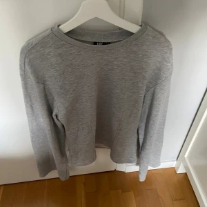 Grå sweatshirt från 157, storlek M - En stilren grå sweatshirt från 157 i storlek M. Tröjan har rund halsringning och långa ärmar, perfekt för en chill och enkel look. Tillverkad i mjuk bomullsmix som känns skön mot huden. Passar dig som gillar basic och minimalistisk stil.