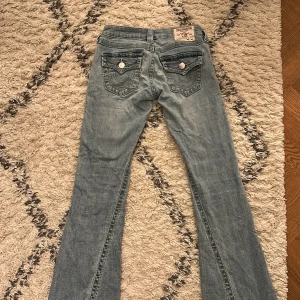 True Religion Joey ljusblå flare jeans - Säljer ett par ljusblå True Religion Joey jeans med låg midja och flare-ben. Klassiska fickor med snygga sömmar och silverfärgade knappar. Jeansmaterialet är mjukt och har en cool tvättad look. De är inte alls slitna utan i toppskick!