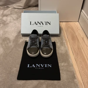 Lanvin captoe ljusblå sneakers i mocka - Snygga sneakers från Lanvin i ljusblå mocka med svart snörning och mörkgrön lackad tå. Skorna har vit sula. Perfekta för dig som gillar en stilren men ändå unik look. Det är storlek 6 uk men är betydligt mycket större passar 40.Det finns några defekter som du ser på bild 2 på hälen av högra skon där det är ett märke och även i mockan på olika ställen är den lite dålig men det är inget som syns när man går runt med dem. Box och dustbag finns. Har du frågor är det bara att höra av sig. MVH Samuel😊