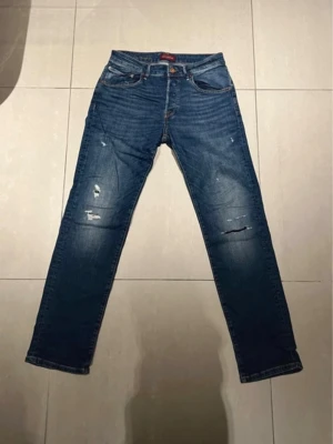 Jack and Jones jeans - Säljer ett par klassiska Jack and Jones jeans i blå denim. Modellen har normal passform med raka ben och slitna detaljer framtill för en cool, avslappnad look. Femficksmodell med Jack and Jones -lapp bak i midjan. Perfekta till sneakers eller  boots.