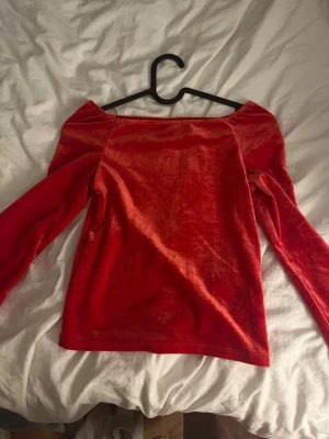 Röd sammetstopp offshoulder Kappahl - Säljer en röd offshoulder topp från Kappahl i mjuk sammet. Toppen har lång ärm och en snygg, rak urringning som ger en trendig vibe. Perfekt att styla med jeans eller kjol för en cool look.