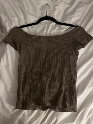 Brun ribbad topp från 157 - Säljer en brun ribbad topp från 157 med korta ärmar och off shoulder-modell. Toppen har en stretchig, skrynklig struktur och är tillverkad i ett mjukt material som sitter tajt mot kroppen. Perfekt för dig som gillar en enkel men trendig stil.