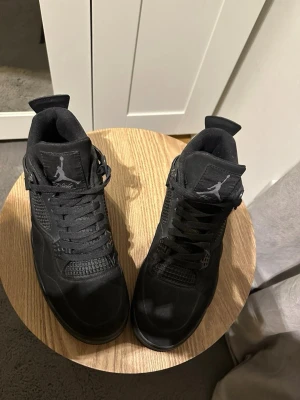 Svarta Nike Jordan 4 sneakers - Säljer ett par helsvarta Nike Jordan 4 sneakers med klassisk meshpanel, snörning och Jumpman-logga på plösen. Skorna har en robust sula och är tillverkade i mocka och syntetmaterial för en clean och stilren look. Kom privat om du vill diskutera pris