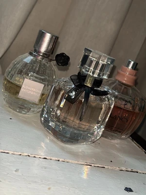 Parfymtrio: Flowerbomb, Mon Paris, La Vie Est Belle - Säljer tre ikoniska parfymer: Flowerbomb från Viktor & Rolf i rund glasflaska med silverdetaljer (40-45 %) ,  Mon Paris från Yves Saint Laurent i elegant fyrkantig flaska med svart rosett (90 %), samt La Vie Est Belle från Lancôme i mjukt rosa glasflaska med silvrig kork (70-65 %)  Alla flaskor har snygg design och feminina dofter.  Har försökt skriva ut hur mycket som finns i flaskorna. Rensar då jag inte hinner använda allting tyvärr 💕 säljer allt ihop för priset som står 🩷🩷🥰