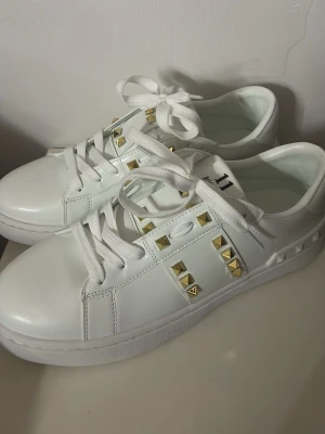 Valentino Rockstud sneakers - Snygga vita Valentino Rockstud sneakers med guldfärgade nitar längs sidorna. 🤍Storlek 41, skorna är oanvända. Perfekta för dig som vill ha en exklusiv och trendig look.😍