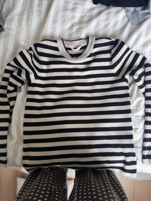 Randig stickad tröja  - Säljer en svart och beige stickad tröja från .object med klassiskt horisontellt randigt mönster. Tröjan har rund halsringning och långa ärmar. Perfekt för dig som gillar en tidlös och enkel stil.