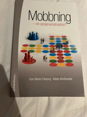 Mobbning – en social konstruktion? - Kursbok om mobbning som socialt fenomen, skriven av Gun-Marie Frånberg och Marie Wrethander. Omslaget är grått med färgglada spelpjäser och prickar. Boken tar upp olika perspektiv på mobbning i skolan och riktar sig till blivande lärare, pedagoger och socionomer. Fint skick men använd, markeringar finns se bild