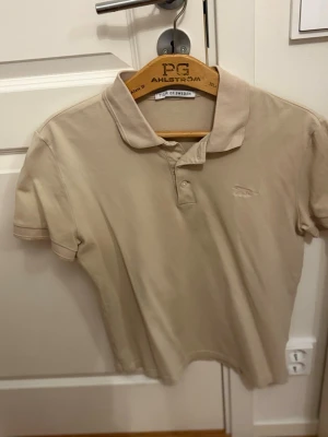 Beige och grön pikétröja Tiger of Sweden - Två klassiska pikétröjor från Tiger of Sweden i beige och grön färg. Båda har krage, korta ärmar och diskret broderad logga på bröstet. Perfekta för en clean och stilren look. Materialet är mjuk bomull som känns skönt mot huden.