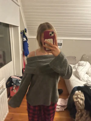 Grå off shoulder stickad tröja - Mysig grå stickad tröja med off shoulder-design och vida ärmar. Tröjan har en bred krage som kan bäras nedanför axlarna för en avslappnad och trendig look. Perfekt för dig som gillar en chill och stilren vibe.