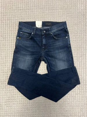 Tiger of Sweden blå jeans W30 L32 - Snygga blå jeans från Tiger of Sweden med klassisk femficksdesign och diskret logga vid fickan. Jeansen har en smal passform och är tillverkade i slitstarkt denimtyg. Perfekta för dig som gillar stilrena och tidlösa jeans. Aldrig använda