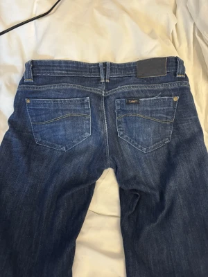 super low waist jeans - Snygga super lågmidjade blåa utsvängda jeans från Lee. Har bara används ett fåtal gånger. Säljer för att de är för små för mig och används knappast. Innerbens längden är 80cm och höfterna är ungefär 41 cm breda. midjan är 12 cm lång, alltså ungefär 2 cm längre än ett kreditkort❤️ Har även sprätt upp dem längst ner vid benen men det syns knappast när man har på sig dem❤️