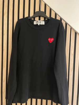 Svart långärmad tröja Comme des Garçons - Svart långärmad tröja från Comme des Garçons PLAY med det ikoniska röda hjärtat med ögon broderat på bröstet. Tröjan har rund halsringning och är tillverkad i mjukt bomullstyg. Perfekt för en stilren och trendig look. Tröjan är i S storlek, men den passar mer XS.