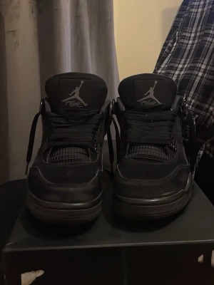 Svarta Nike Jordan 4 sneakers - Säljer ett par helsvarta Nike Jordan 4 sneakers med klassisk Jumpman-logga på plösen och hälen. Skorna har snörning, meshdetaljer och en robust sula. Perfekta för dig som gillar stilrena och ikoniska sneakers.