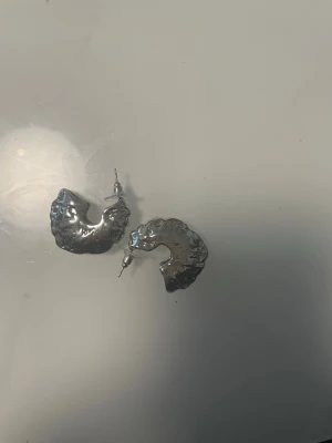 Chunky silvriga örhängen i oregelbunden form - Säljer ett par chunky örhängen i blankt silverfärgat metallmaterial. De har en cool, oregelbunden och lite skulpterad form som verkligen sticker ut. Perfekta för dig som gillar statement-smycken och vill ha något unikt i smyckeslådan.