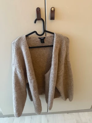 Beige stickad kofta från Lindex - Mysig beige stickad kofta från Lindex i öppen modell. Koftan har långa ärmar och en avslappnad passform, perfekt att slänga över en t-shirt eller topp. Materialet är mjukt och ger en chill vibe till din outfit.