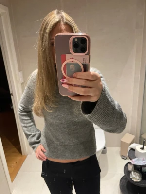 Grå stickad tröja i klassisk modell - En enkel och stilren grå stickad tröja med figursydd midja och utsvänga armar. Perfekt att matcha med jeans eller kjol för en avslappnad look.