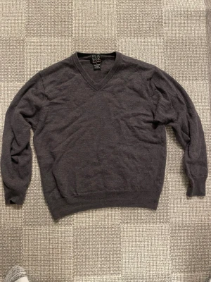 Mörkgrå merinoullströja V-ringad - OBS jag har tvättat tröjan för varmt och då har den krympt från L till S. Snygg mörkgrå stickad tröja från Jos. A. Bank Signature Collection i 100% merinoull. Klassisk V-ringning och ribbade muddar vid ärmslut och nederkant. Perfekt för dig som gillar stilrena och bekväma plagg.