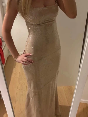 Glittrig champagnefärgad långklänning - Säljer en super fin champagnefärgad klänning med glittriga paljetter. Klänningen är figursydd i passform, klänningen är från babyboo och i storleken XS, är endast testad så prislappen sitter kvar.